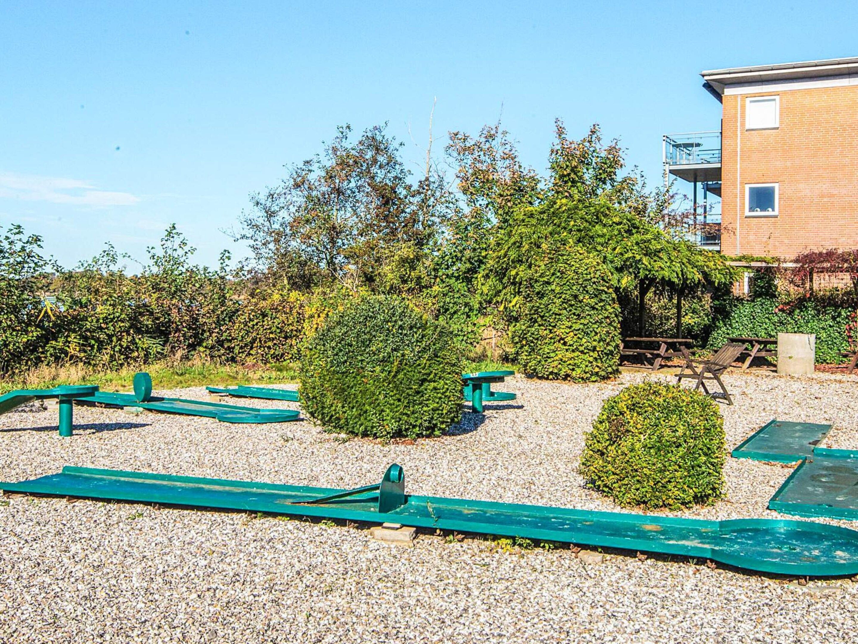 A gravel outdoor area with exercise equipment, a building, and a hedge.