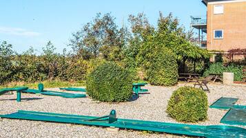 A gravel outdoor area with exercise equipment, a building, and a hedge.
