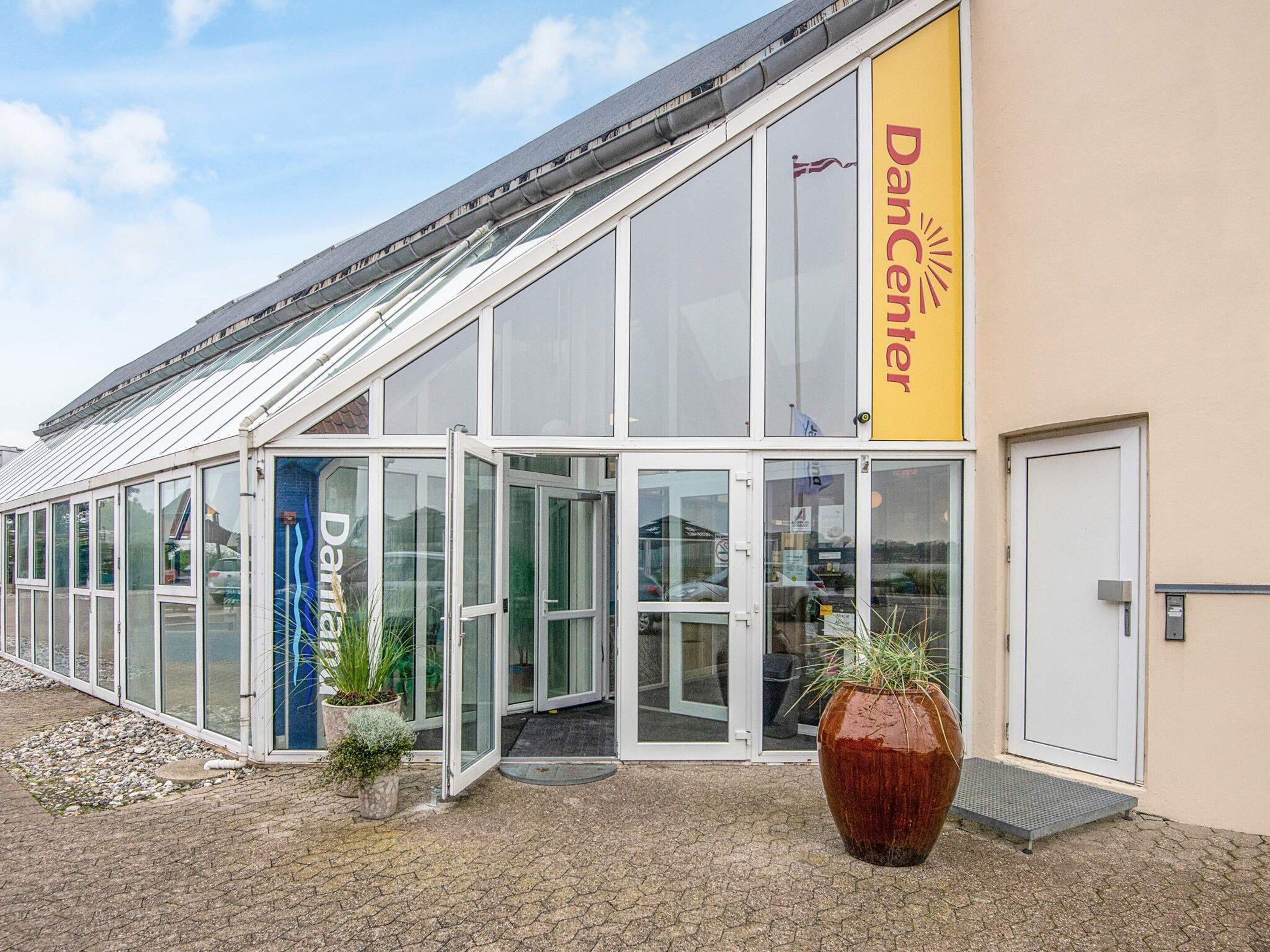 A building with a glass entrance, a yellow sign reading 'Dancenter,' and a large potted plant in front.
