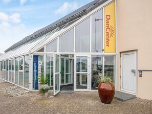 A building with a glass entrance, a yellow sign reading 'Dancenter,' and a large potted plant in front. - 4 Person Holiday Home in Hejls (Hejls)