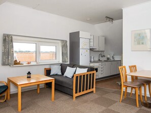 A compact living space with a sofa, a dining table, a kitchen area, and a window with a view.