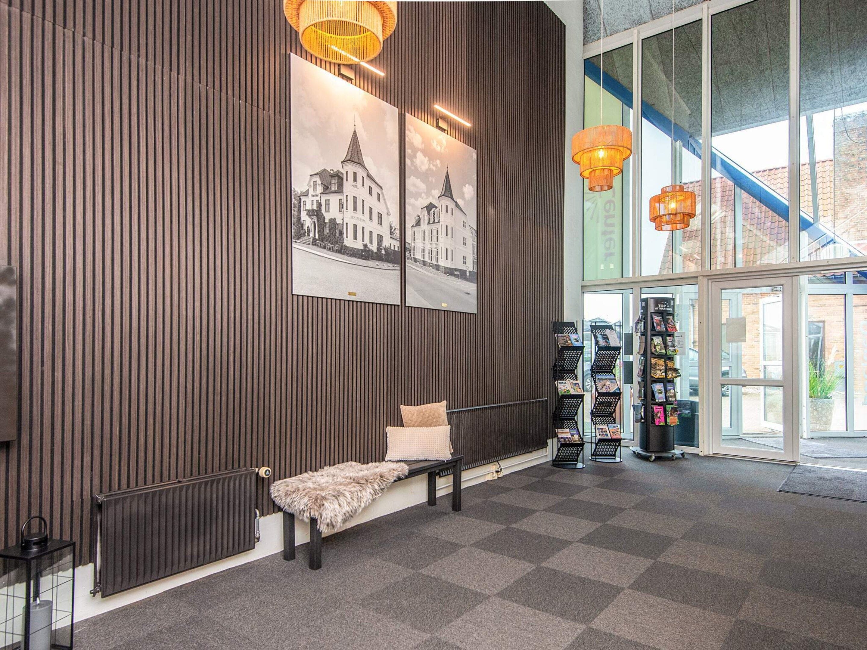 A reception area with a bench, a radiator, a wall-mounted shelf with magazines, and a large window.