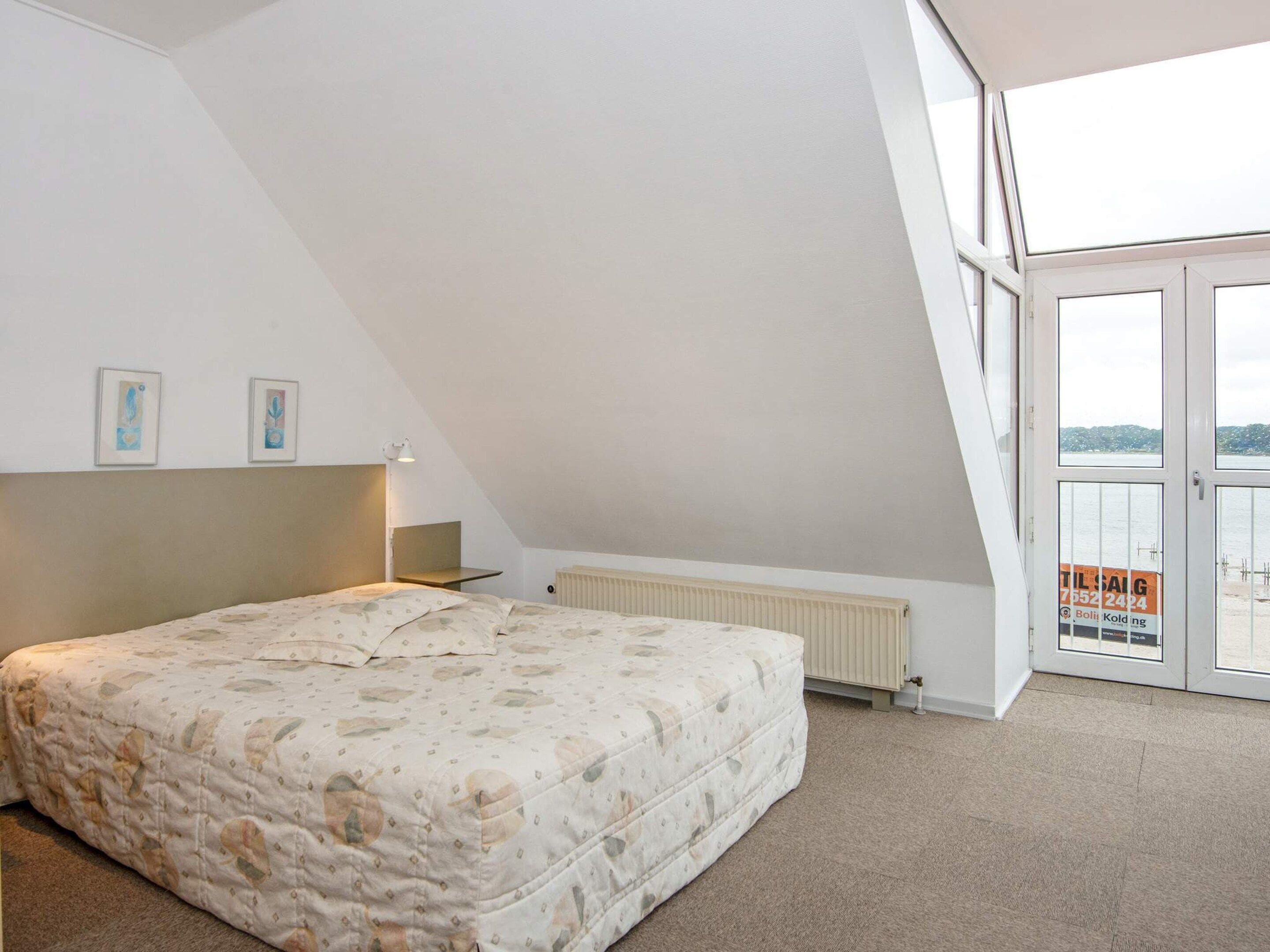 Un dormitorio con cama, radiador, escritorio y ventana con vista al mar.