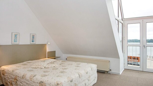 A bedroom with a bed, a radiator, a desk, and a window with a view of the sea. - 4 Person Holiday Home in Hejls (Hejls)