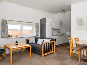 A compact living space with a sofa, a dining table, a kitchenette, and a window with a view.