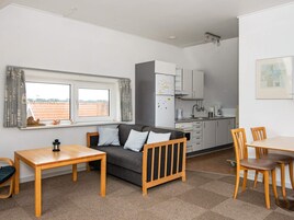 A compact living space with a sofa, a dining table, a kitchenette, and a window with a view.