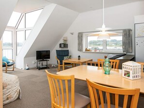 Ein moderner, gut beleuchteter Raum mit Esstisch, Stühlen, Fernseher und einem Fenster mit Vorhängen.