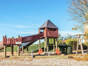 Un parque infantil con un tobogán, una estructura para escalar y una torre de vigilancia.