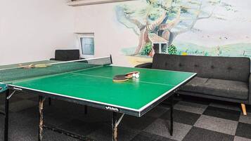 A ping pong table with a net, a sofa, and a mural of a tree on the wall.