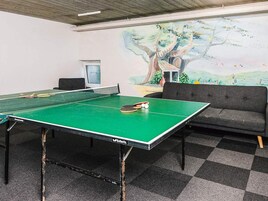 Una mesa de ping pong con red, un sofá y un mural de un árbol en la pared.