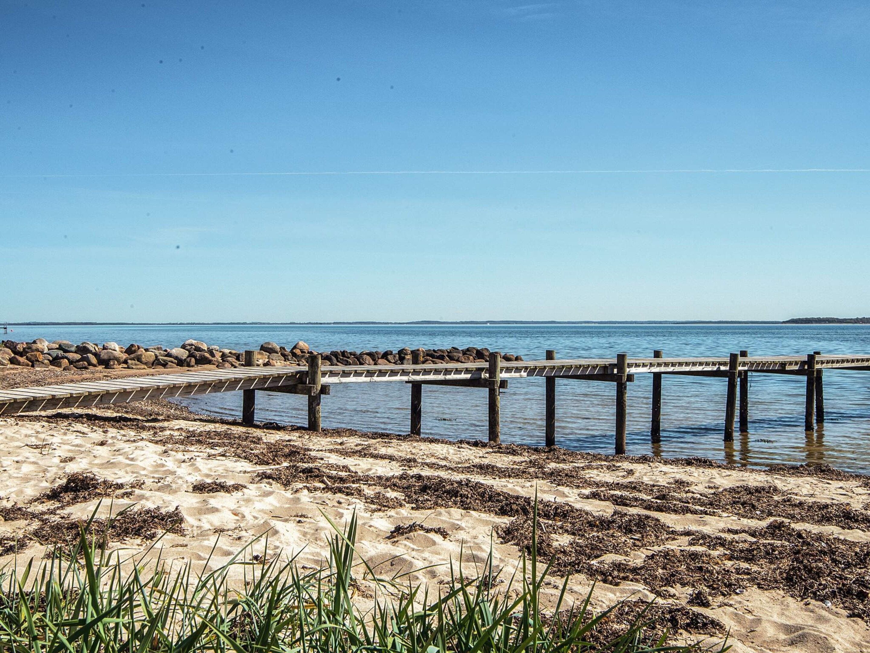 A wooden pier extending into calm waters, surrounded by a sandy beach with sparse vegetation.