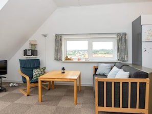 A compact living space with a sofa, a small table, a chair, a television, and a window with curtains. - 4 Person Holiday Home in Hejls (Hejls)