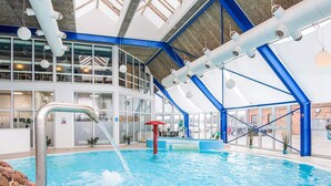 An indoor swimming pool with a high ceiling, skylights, and a blue and white color scheme. - 4 Person Holiday Home in Hejls (Hejls)