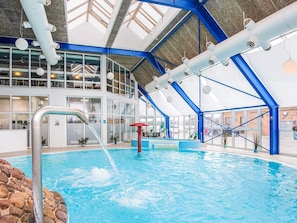 Una piscina interior con techos altos, tragaluces y una decoración en tonos azul y blanco.