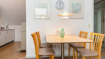 A dining area with a table and four chairs, a clock, and two framed artworks on the wall.