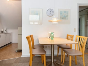 A dining area with a table and four chairs, a clock, and two framed artworks on the wall. - 4 Person Holiday Home in Hejls (Hejls)