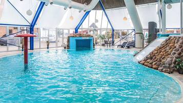 An indoor swimming pool with clear blue water, a rock wall, and a slide.