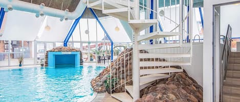 An indoor swimming pool with a stone wall, a white staircase, and a blue ceiling.