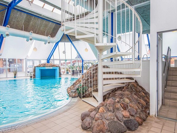An indoor swimming pool with a stone wall, a white staircase, and a blue ceiling.