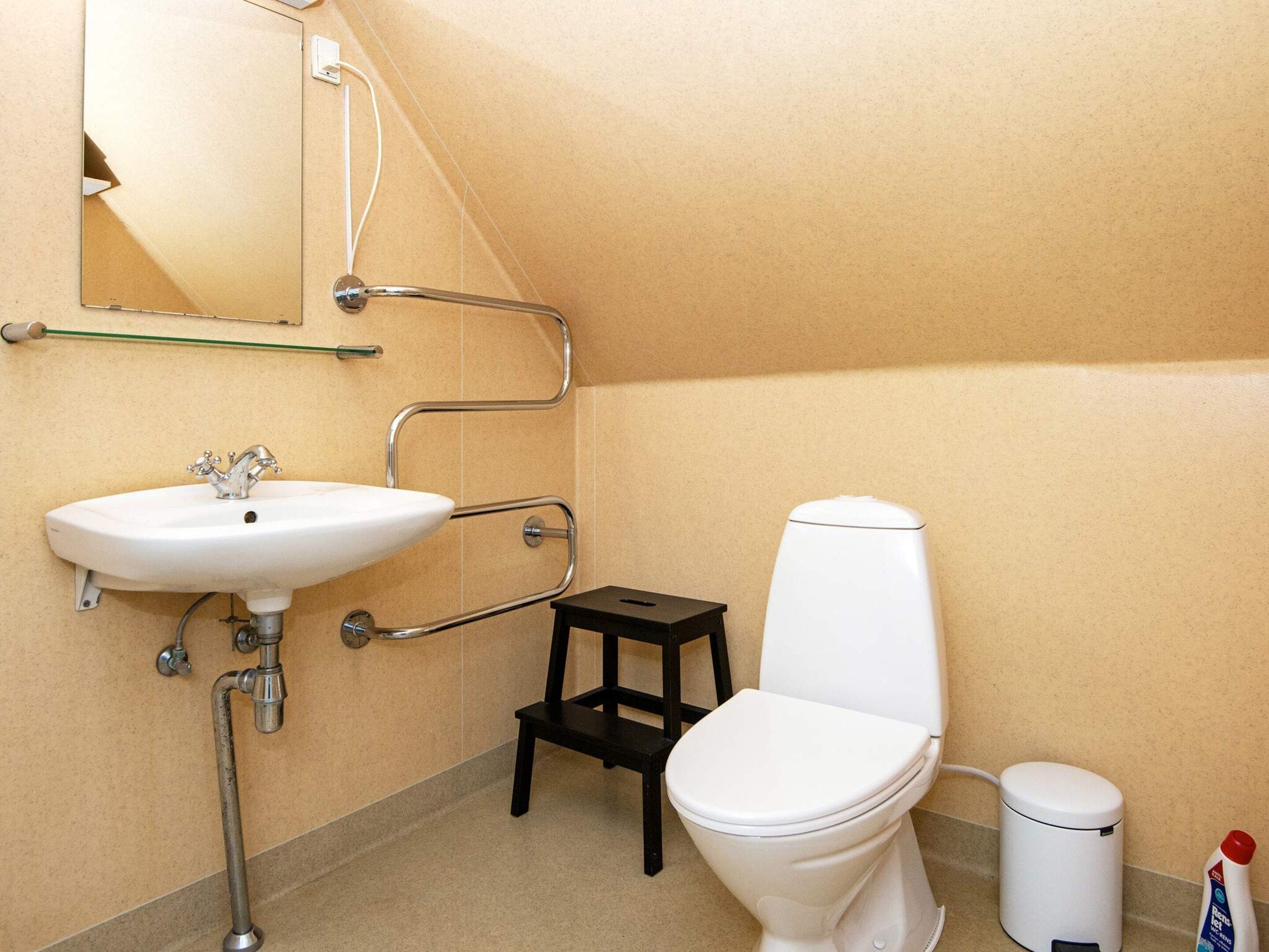 Een badkamer met een wit wastafel, toilet en een klein krukje.