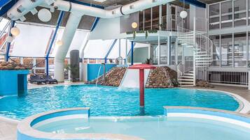 An indoor swimming pool with a slide, a staircase, and lounge chairs.