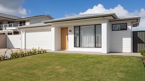 Una casa moderna de dos pisos con un amplio ventanal corredera, un garaje y un césped bien cuidado.