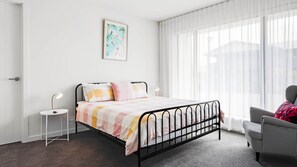 Une chambre à coucher avec un lit, des tables de chevet, une chaise et une fenêtre avec des rideaux légers.