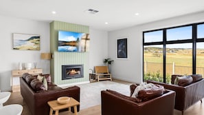 Cozy living room with a fireplace, comfortable seating, and artwork on the walls, offering a view of the countryside.