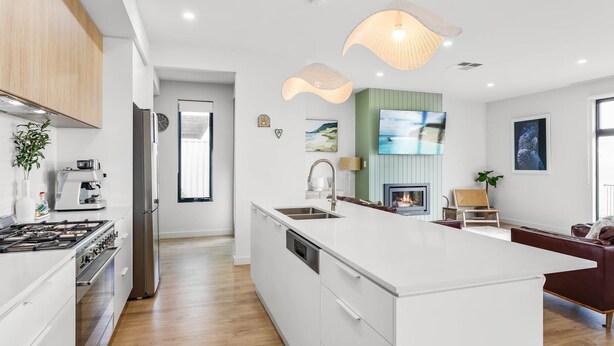 Una cocina moderna con una isla central, un comedor con chimenea y una sala de estar con televisor grande.