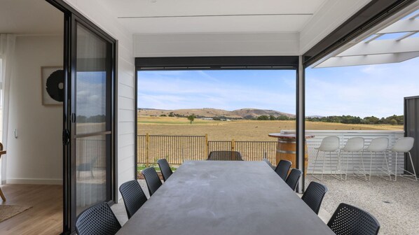 Enjoy meals at the large dining table surrounded by comfortable chairs, with a view of the rolling hills from the adjacent balcony.