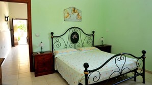 Un dormitorio con cama, mesitas de noche, una lámpara de pared y una puerta que da a otra habitación.