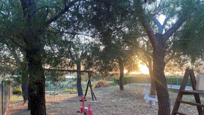 Un parque infantil con columpios y un tobogán, rodeado de árboles y una valla.