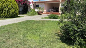 Una casa con porche cubierto, un sendero de grava y abundante vegetación.