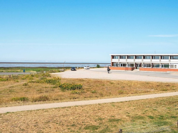 Um edifício com telhado plano e janelas amplas, situado perto de uma praia sob um céu claro.