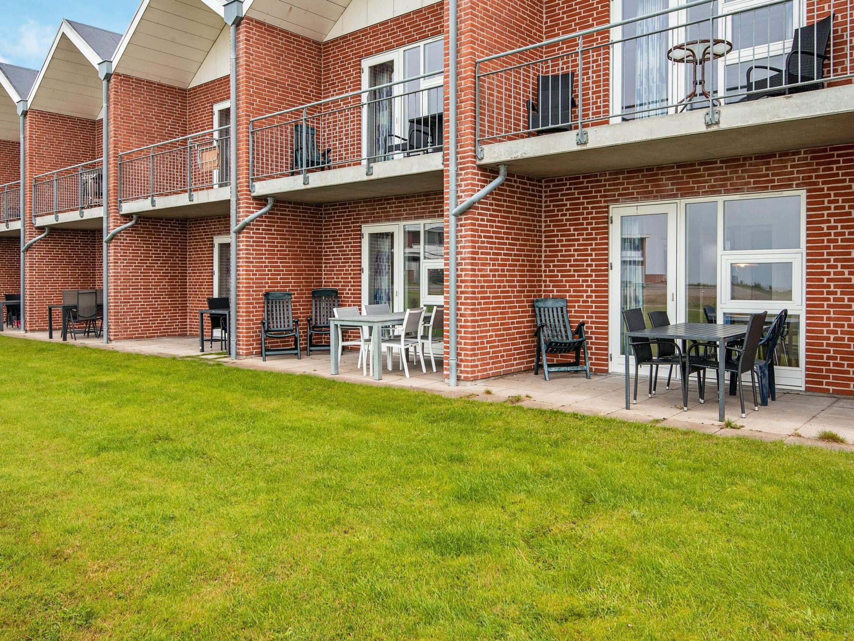 A row of brick apartment buildings with balconies, outdoor seating areas, and a grassy lawn.