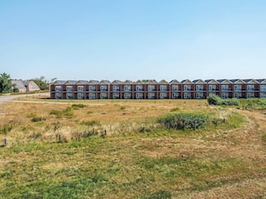 Een rij herenhuisjes van baksteen met meerdere balkons, een gazon ervoor en een heldere lucht.