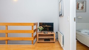 Ein Zimmer mit einem hölzernen Bett, einem Fernseher auf einem Holzschrank, einem Heizkörper und einer Tür zu einem anderen Raum.