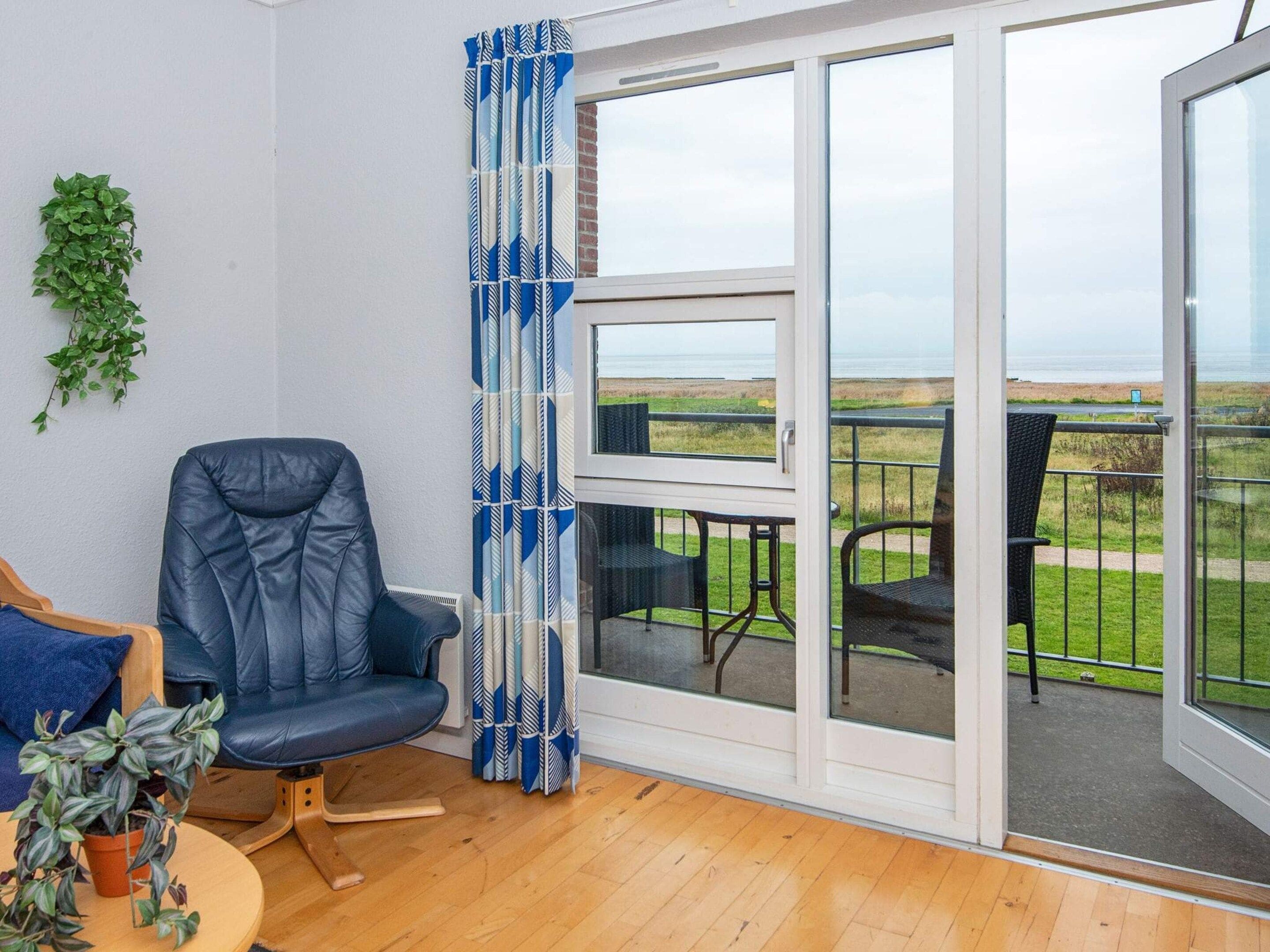 A room with a blue leather chair, a small table with a plant, and a view of a grassy area through a glass door.