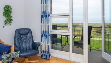 A room with a blue leather chair, a small table with a plant, and a view of a grassy area through a glass door.