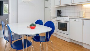 Eine moderne Küche mit weißen Schränken, einem weißen Esstisch mit blauen Stühlen, einer roten Schale mit einer Pflanze und einer Pendelleuchte.