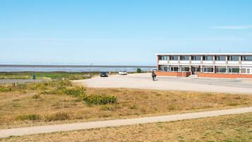 A building with a flat roof and large windows, situated near a beach with a clear sky.
