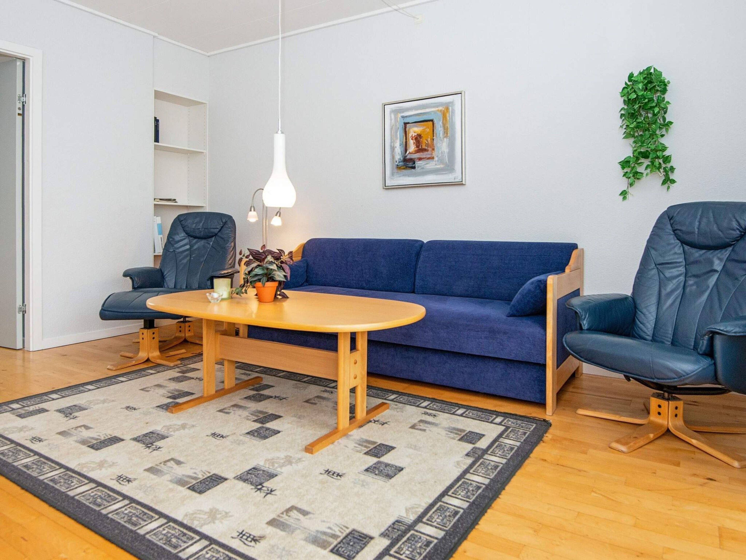 Ein modernes Wohnzimmer mit einem blauen Sofa, zwei schwarzen Ledersesseln, einem Holztisch und einem gemusterten Teppich.