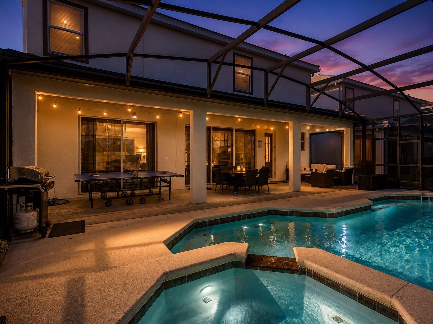 A poolside area with a table and chairs, a grill, and a covered patio.