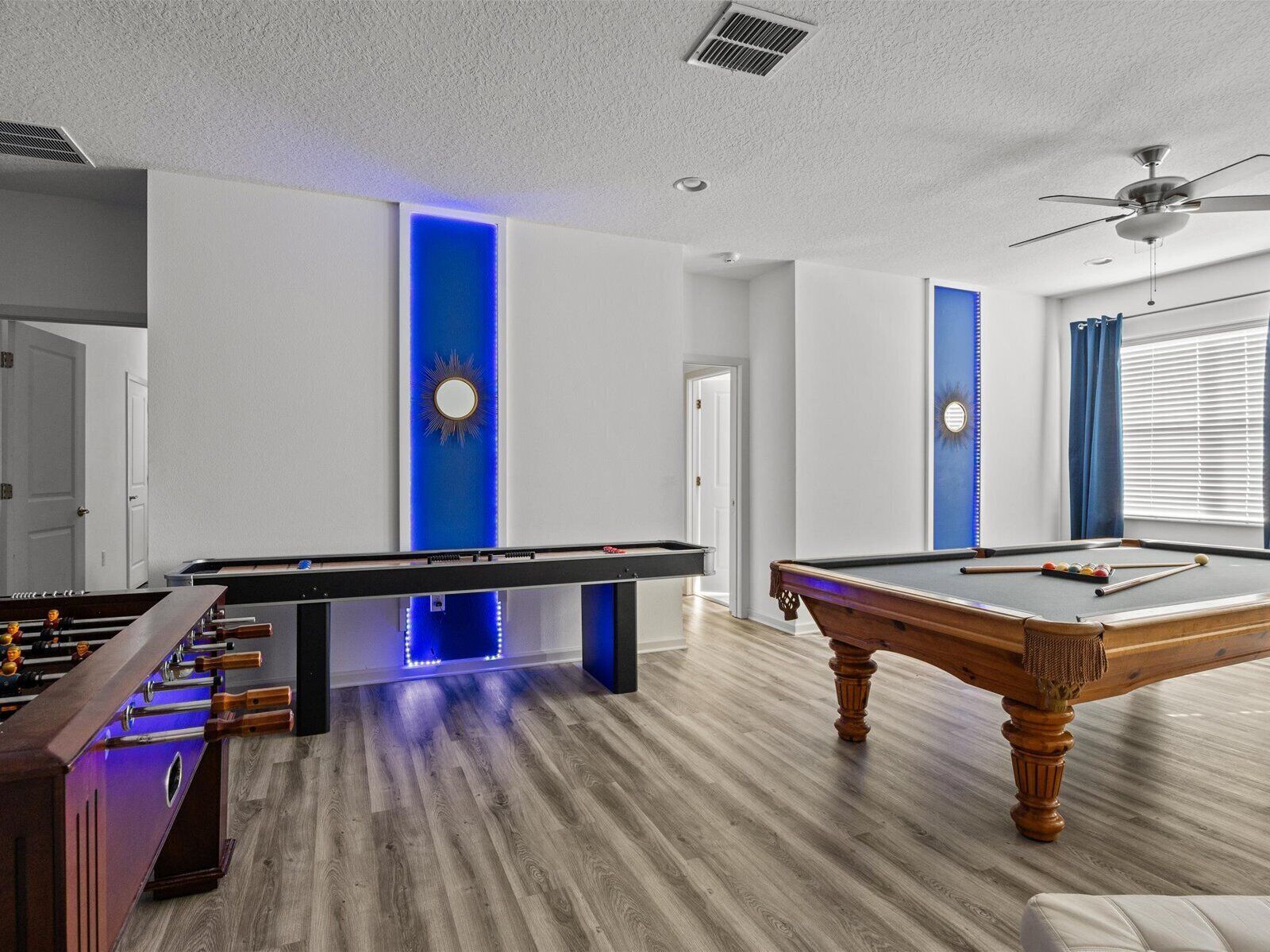 A room with a pool table, foosball table, and a ceiling fan.