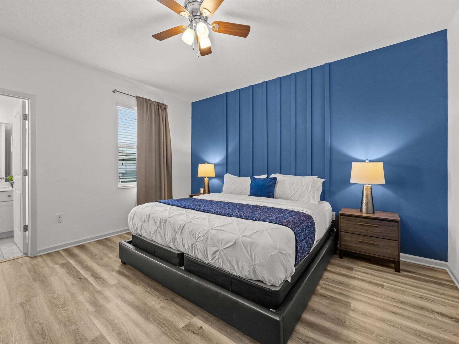 Ett modernt sovrum med en säng, två sänglampor, en takfläkt och ett fönster med gardiner.
