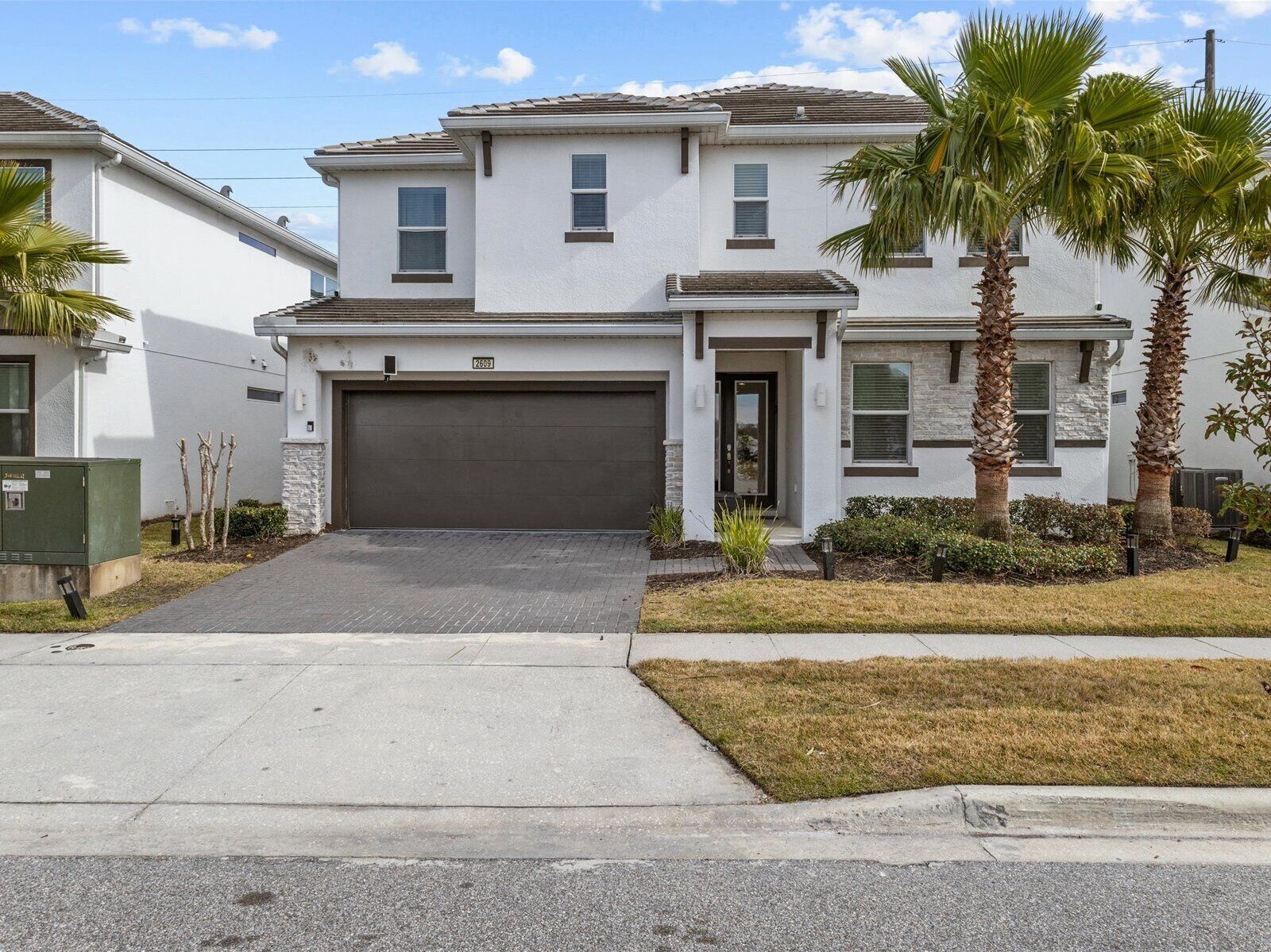 A two-story residential building with a garage, palm trees, and a well-maintained lawn.