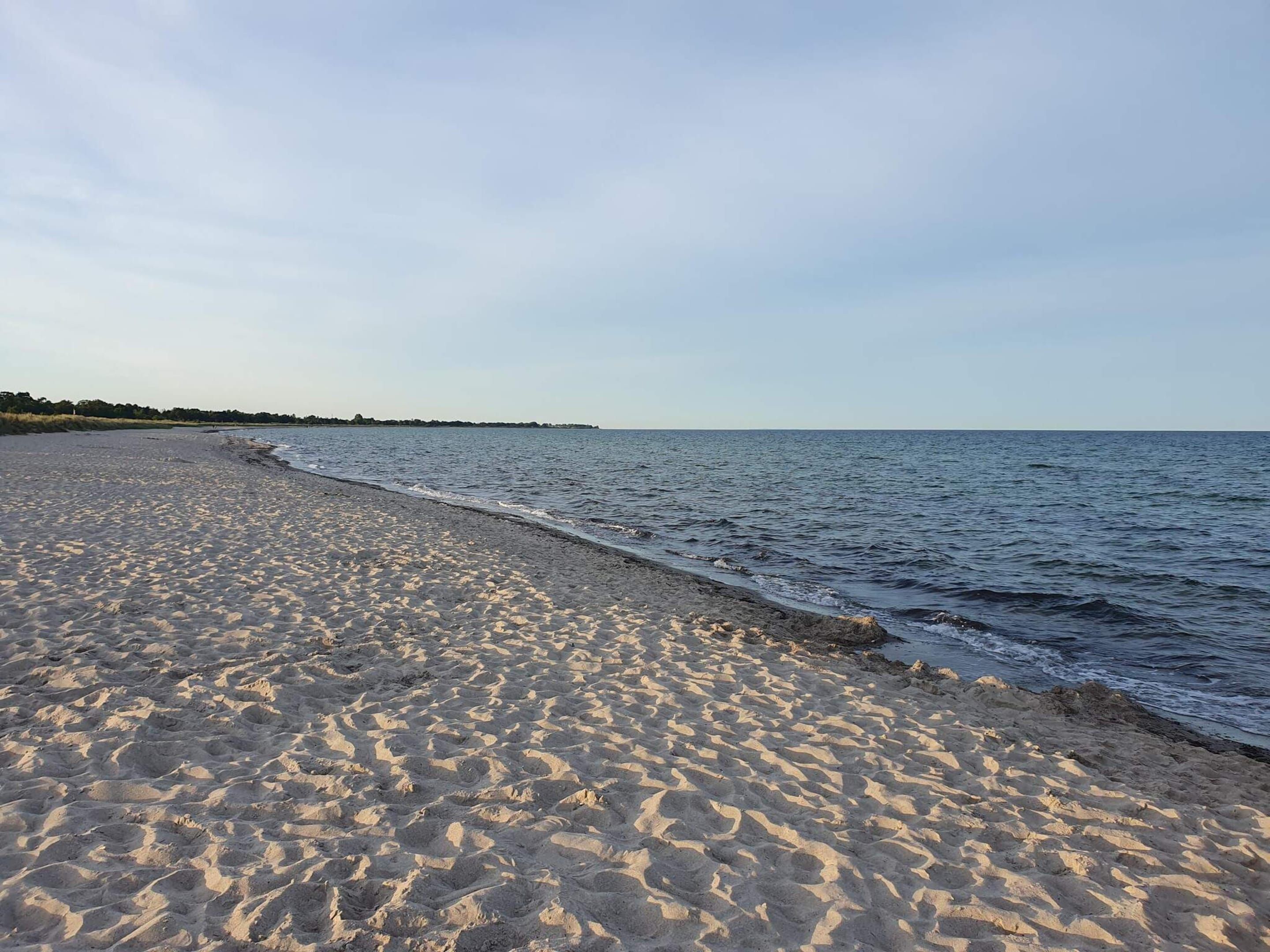 A sandy beach with gentle waves, a clear sky, and a distant shoreline.