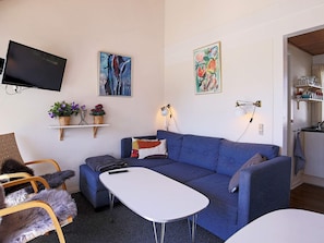 A modern living room with a blue sofa, a white coffee table, and a flat-screen TV mounted on the wall.