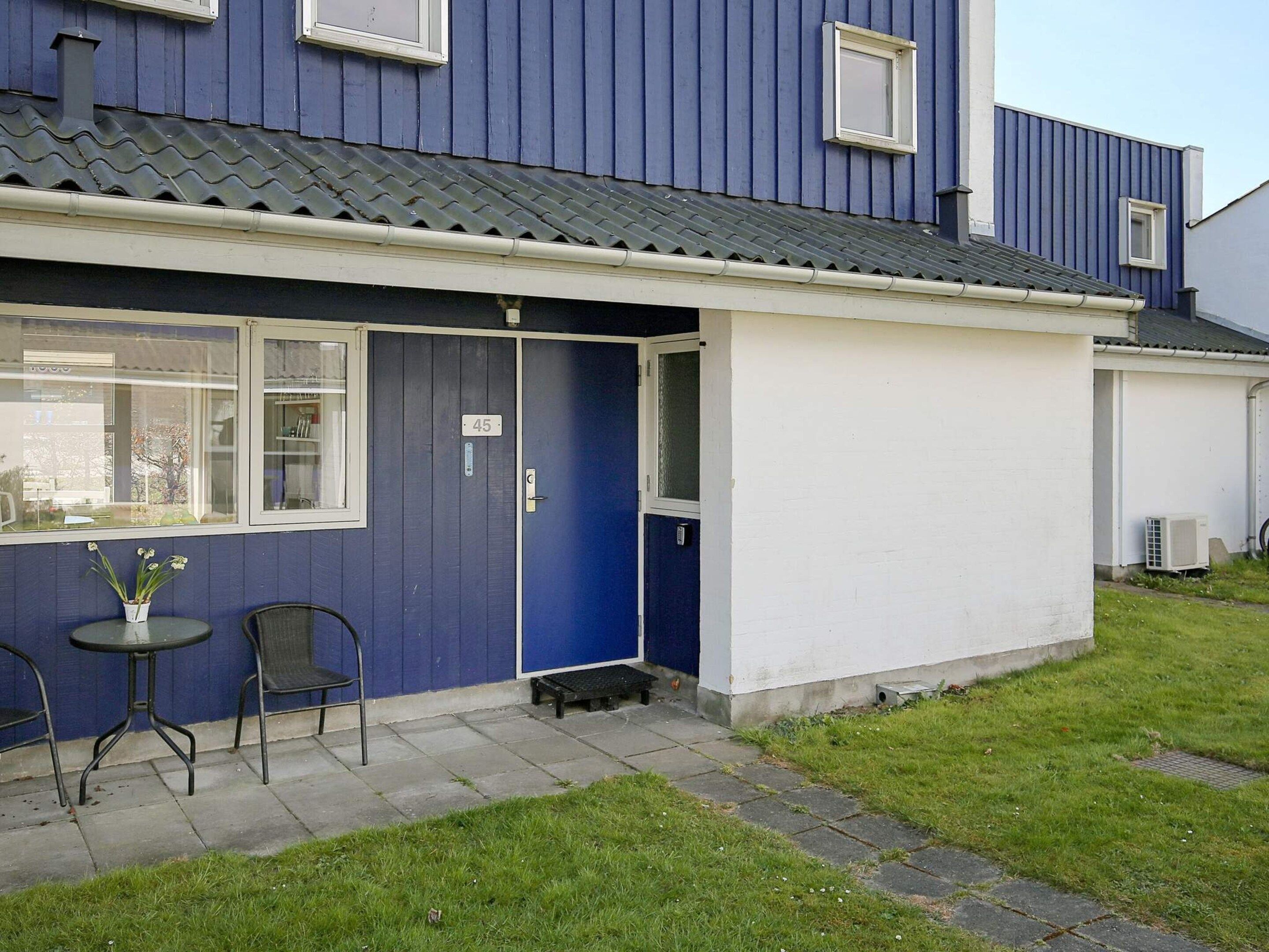 Asuintalo, jonka ulkoseinät ovat siniset, ovi valkoinen ja pieni ulkotila, jossa on kaksi tuolia ja pöytä.
