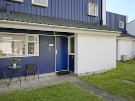 A residential building with a blue exterior, a white door, and a small outdoor seating area with two chairs and a table.